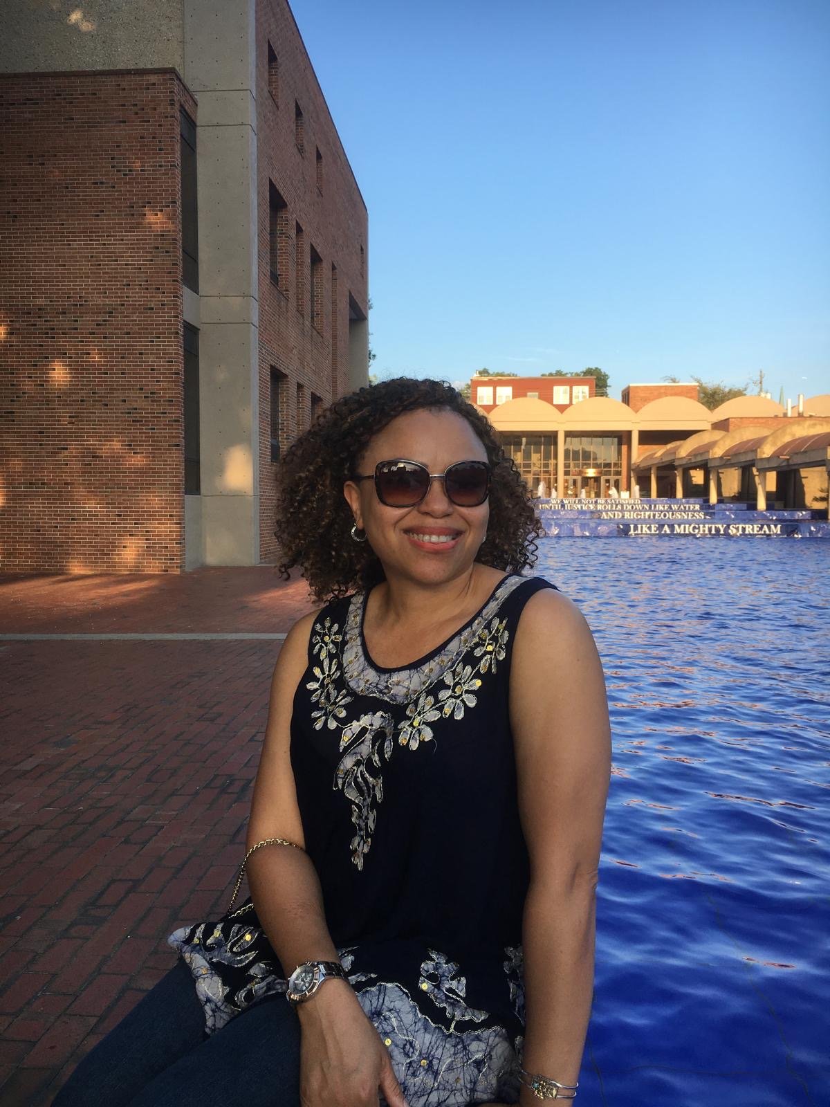 Nonye smiling in the sunshine beside a reflecting pool